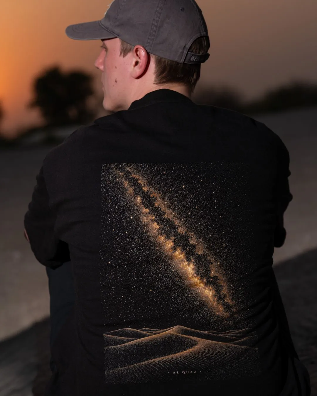 The Al Quaa Galaxy tee from behind at golden hour — the Milky Way print across the back, close. Male model wears M in the Oversized fit.