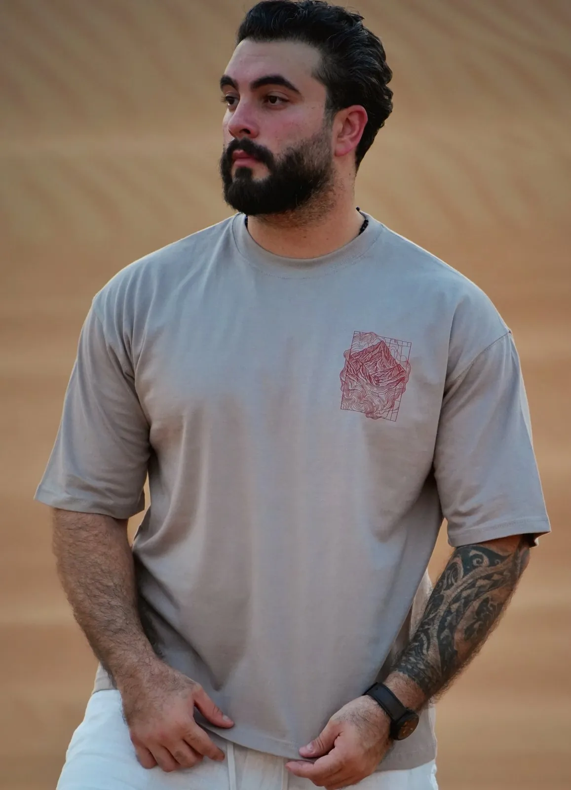 The Hajar Mountains tee worn in the dunes — the contour-line mountain print on the chest
